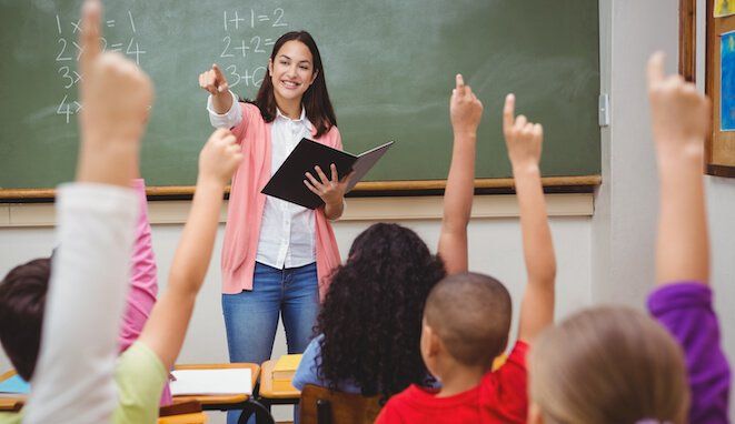 Profesora da clase en una escuela. Los niños levantan la mano. 